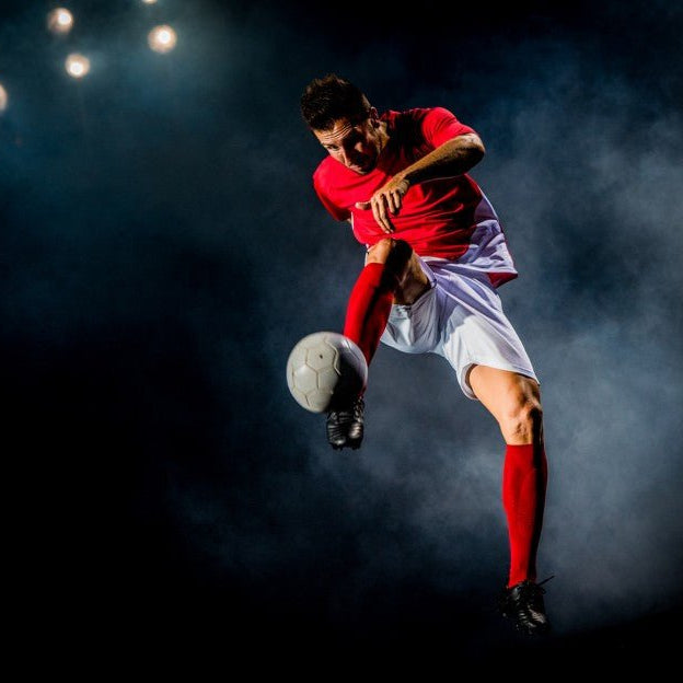Soccer player kicking soccer ball into the air.