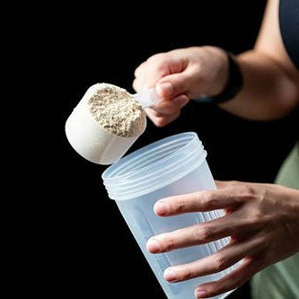 Woman scooping whey protein into a shaker bottle