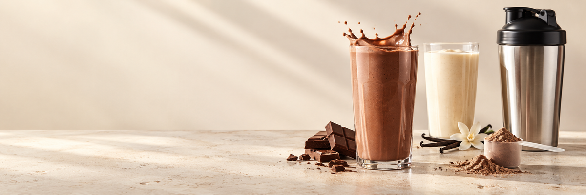Chocolate and vanilla protein shakes with a stainless steel shaker, chocolate pieces and a scoop of powder.